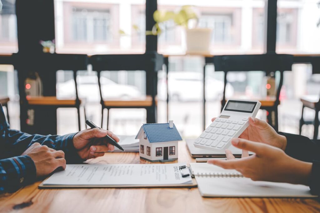 manos en escritorio haciendo cuentas con una casa en miniatura para ley segunda oportundiad hipoteca